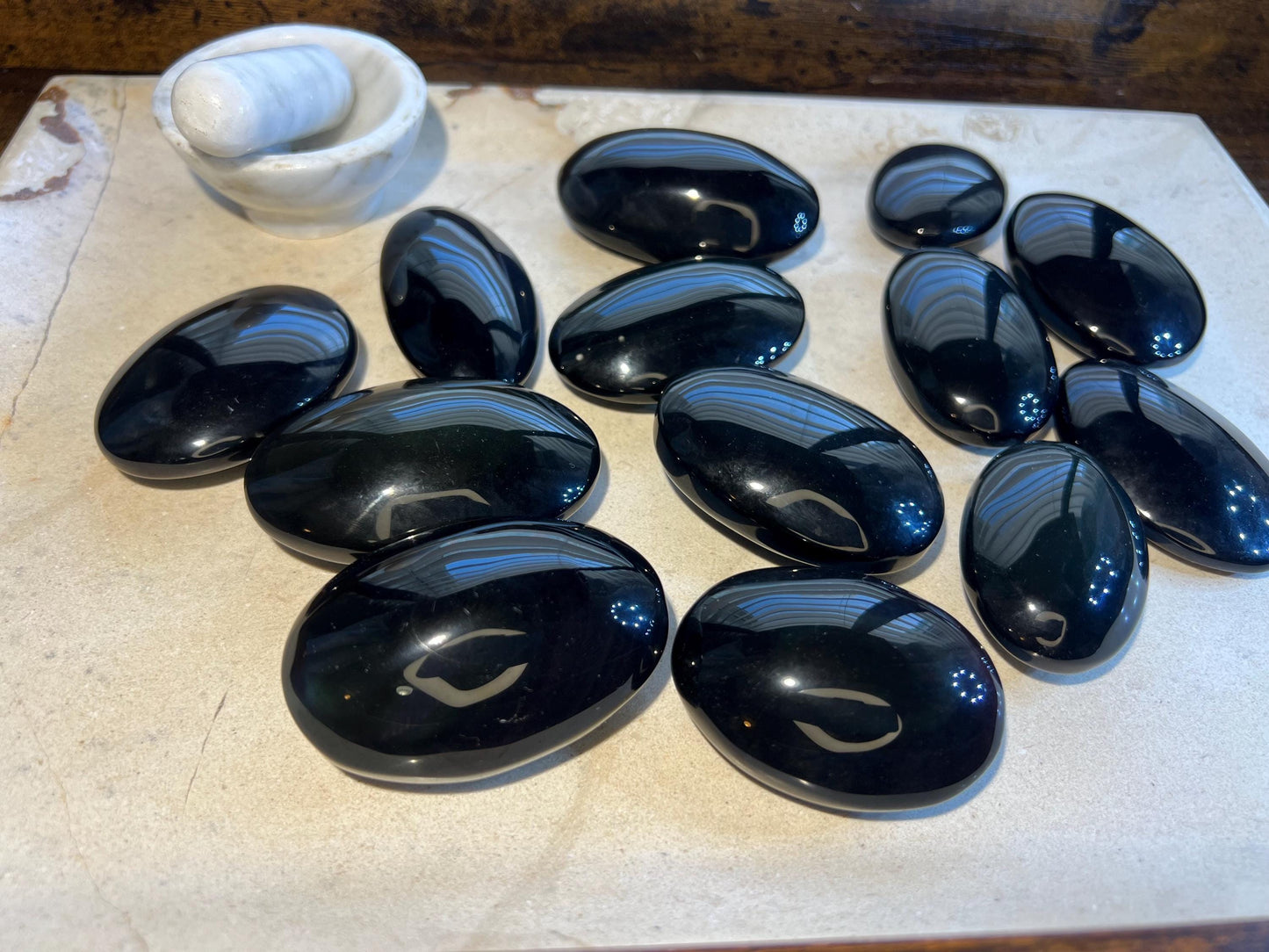 May include: A collection of twelve smooth, black oval-shaped stones. The stones are arranged on a light-colored surface.