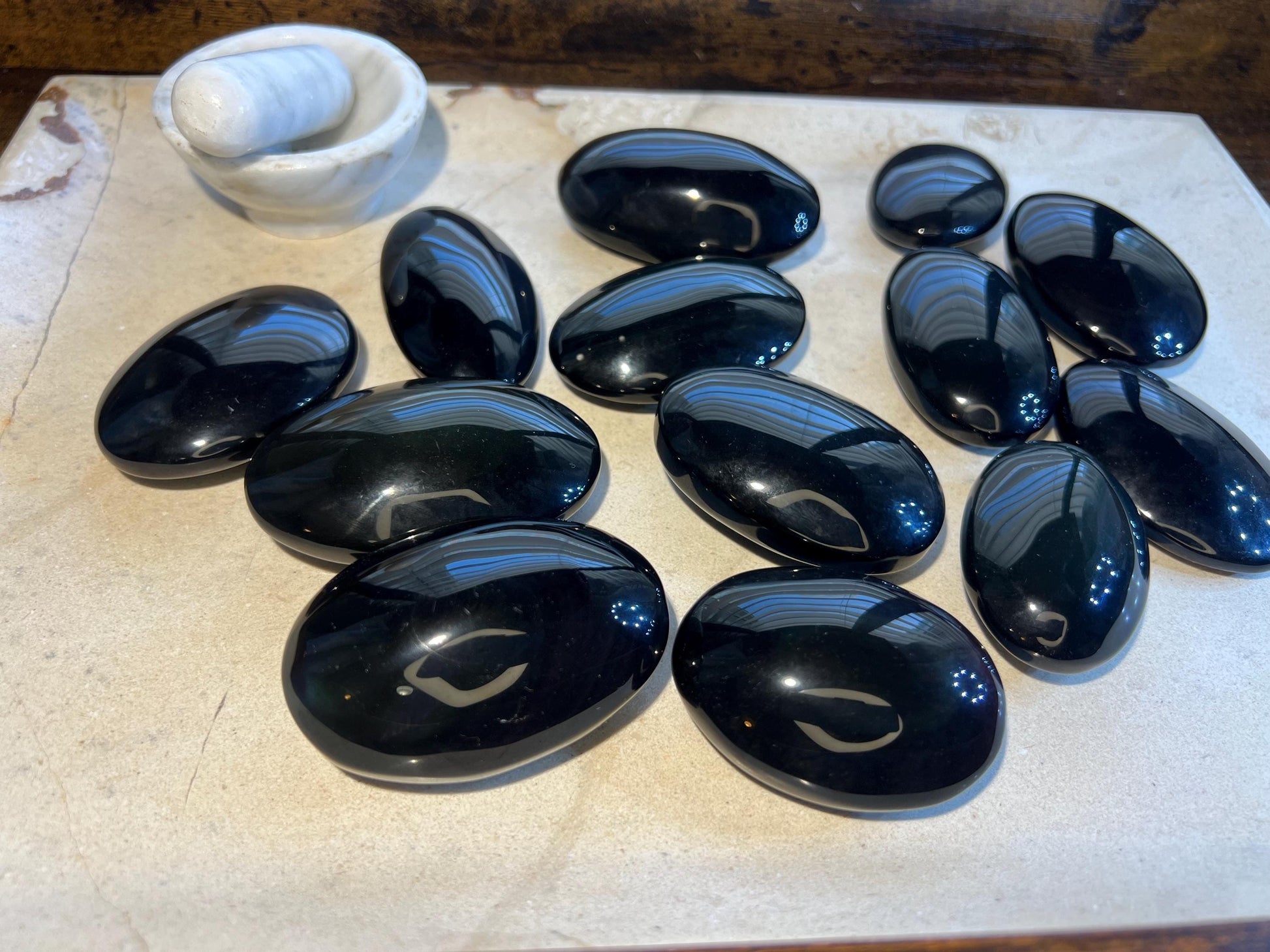 May include: A collection of twelve smooth, black oval-shaped stones. The stones are arranged on a light-colored surface.
